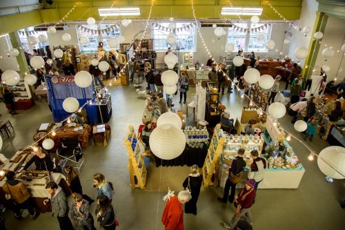 A bustling indoor market with vendors, shoppers, and decorative lanterns hanging from the ceiling.