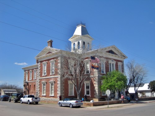 Historic brick building with a tower, American flag, and trees, set against a clear blue sky.