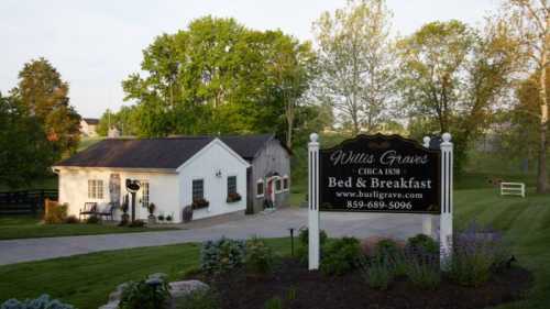 A charming bed and breakfast with a sign, surrounded by greenery and trees, in a peaceful rural setting.