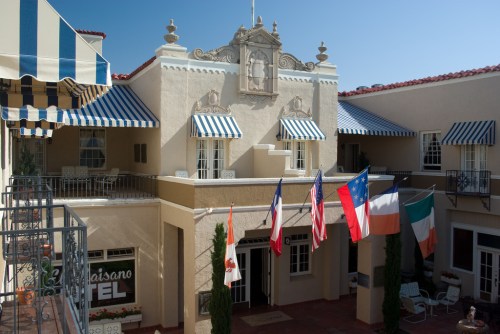 Historic hotel exterior featuring colorful awnings and flags from Texas, the U.S., and other countries. Clear blue sky.