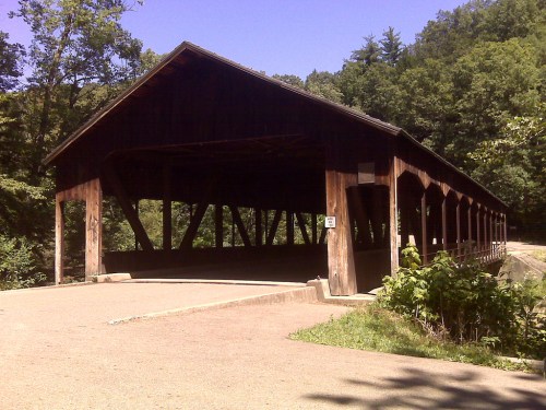 A wooden covered bridge surrounded by trees, with a gravel path leading up to it.