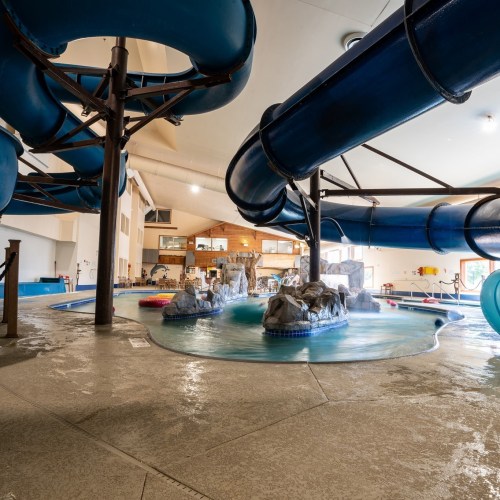 Indoor water park featuring blue slides, a pool, and rock formations, with a bright and spacious atmosphere.