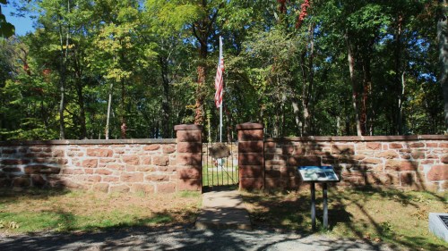 A stone wall with a gate and an American flag, surrounded by trees in a park-like setting.