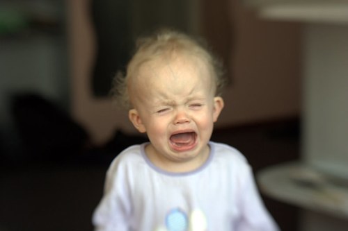 A young child with curly hair is crying, expressing strong emotions in a softly blurred indoor setting.