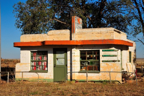 Abandoned building with a colorful facade, featuring green doors and windows, set against a clear blue sky.