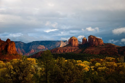 A scenic view of red rock formations and lush greenery under a cloudy sky in a mountainous landscape.