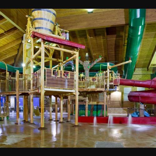 Indoor water play structure with slides, water features, and wooden elements in a spacious, brightly lit area.