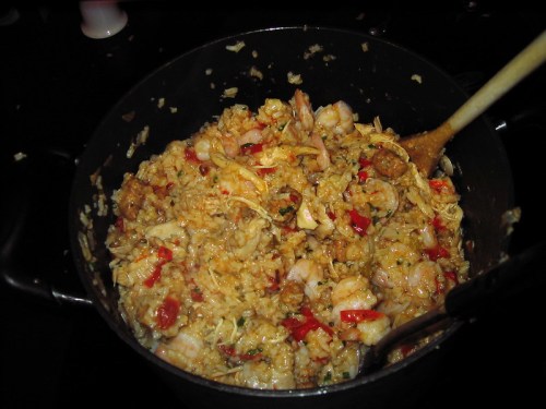 A large pot filled with a colorful mixture of rice, shrimp, chicken, and vegetables, stirred with a wooden spoon.
