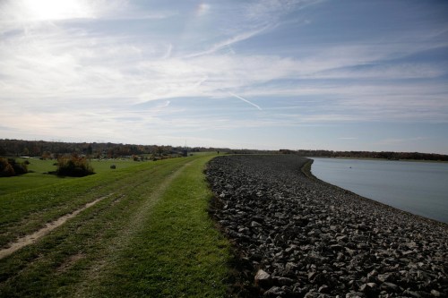 A scenic view of a grassy path alongside a rocky shoreline under a clear sky with wispy clouds.