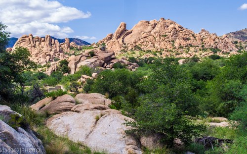 Rocky landscape with large boulders and green vegetation under a clear blue sky.