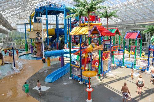 A vibrant indoor water park featuring slides, play structures, and families enjoying the water attractions.