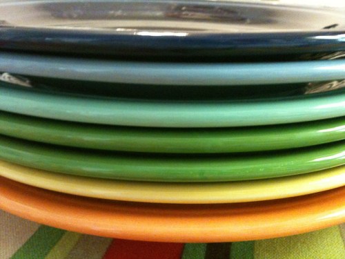 A stack of colorful plates in shades of blue, green, and orange, arranged neatly on a table.