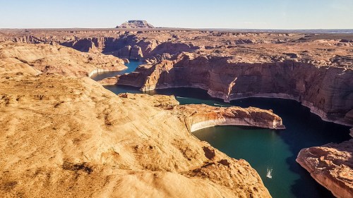 Aerial view of a rugged canyon landscape with winding blue water and rocky cliffs under a clear sky.