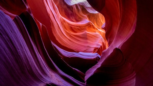 A vibrant, winding canyon with smooth, colorful rock formations in shades of red, orange, and purple.