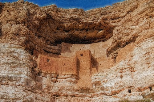 Ancient cliff dwellings carved into a rocky cliff, showcasing earthy tones and a clear blue sky above.