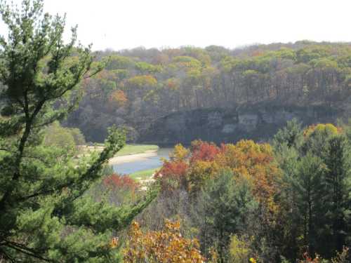 A scenic view of a river winding through colorful autumn trees and hills under a clear sky.