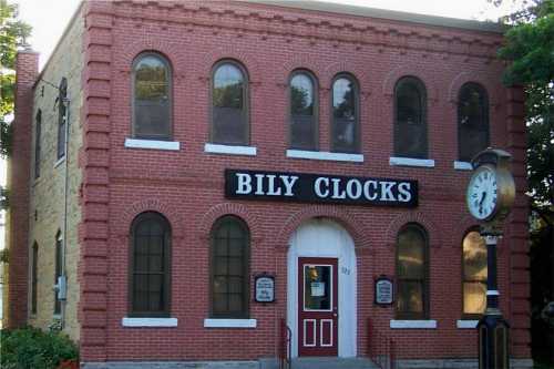 A brick building with large arched windows and a sign reading "BILY CLOCKS," featuring a clock on the side.