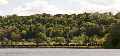 A serene landscape featuring a lake, lush green hills, and a train running along the base of the trees.