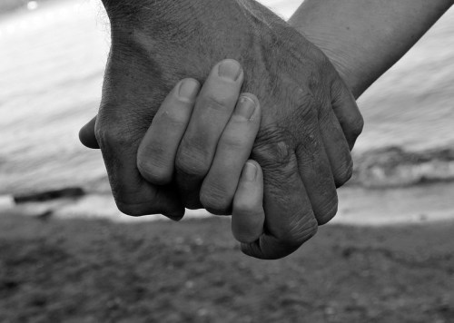 Two hands, one larger and weathered, the other smaller and smoother, clasped together against a beach backdrop.