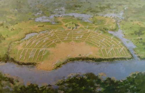 Aerial view of a circular ancient site with pathways and water surrounding it, set in a lush green landscape.