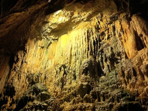 Stalactites and stalagmites in a cave, illuminated by a warm light, showcasing intricate mineral formations.