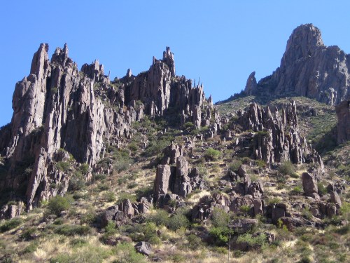 Rocky mountain landscape with jagged peaks and sparse vegetation under a clear blue sky.