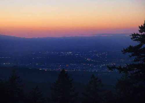 A serene sunset over a city, with soft orange and purple hues in the sky and distant lights twinkling below.