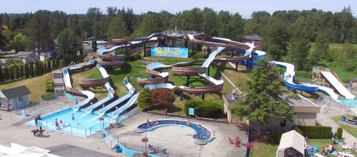 Aerial view of a water park featuring multiple slides, pools, and lush greenery in the background.