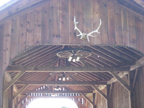 Wooden structure with a high ceiling, featuring antlers and light fixtures hanging from the beams.
