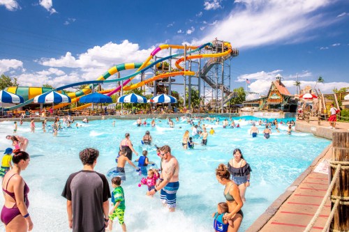 A busy water park scene with colorful slides, a wave pool, and families enjoying the sun and water activities.
