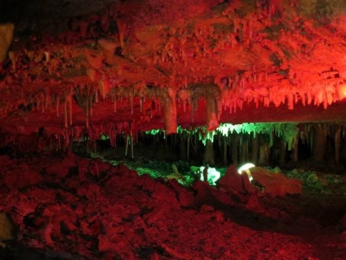 A cave interior illuminated with red and green lights, showcasing stalactites and a rocky floor.