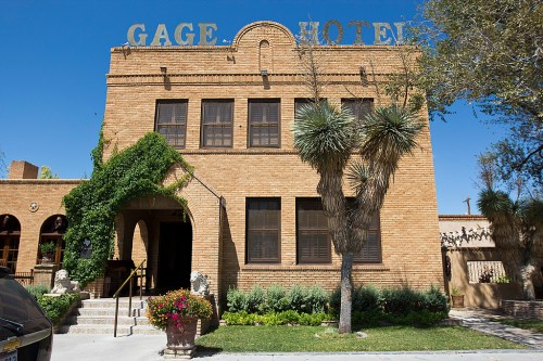 Historic Gage Hotel with a brick facade, large windows, and greenery, set against a clear blue sky.