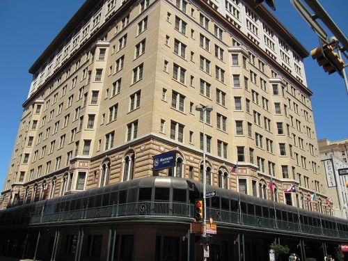 Historic building with a beige facade, multiple stories, and a covered walkway, featuring flags and street signs.
