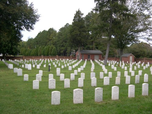 A peaceful cemetery with rows of white gravestones set against a backdrop of trees and a small building.