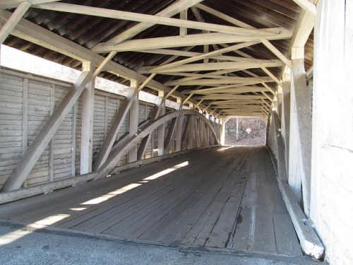 Interior view of a covered bridge, featuring wooden beams and a wooden floor, illuminated by natural light.