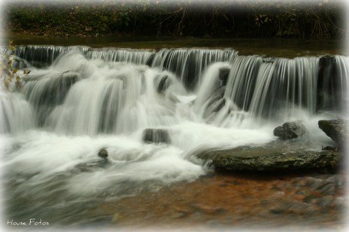 A serene waterfall cascades over rocks, creating a smooth flow of water in a tranquil natural setting.