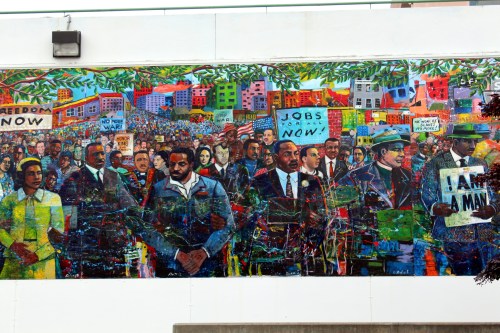 A vibrant mural depicting a diverse group of people marching for civil rights, holding signs for jobs and freedom.