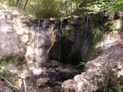 A serene waterfall cascading over rocky terrain, surrounded by lush greenery in a tranquil forest setting.
