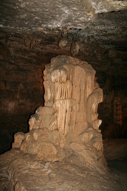 A limestone formation in a dark cave, featuring draped stalactites and a textured, towering structure.