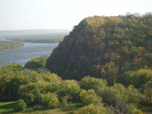 A scenic view of a river winding through lush green and autumn-colored hills under a clear sky.