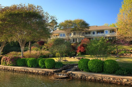 A beautiful lakeside home surrounded by lush gardens and trees, reflecting a serene outdoor setting.
