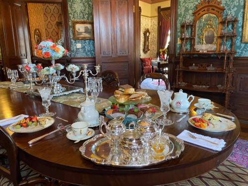 A beautifully set dining table with silverware, tea, pastries, and floral arrangements in an elegant room.