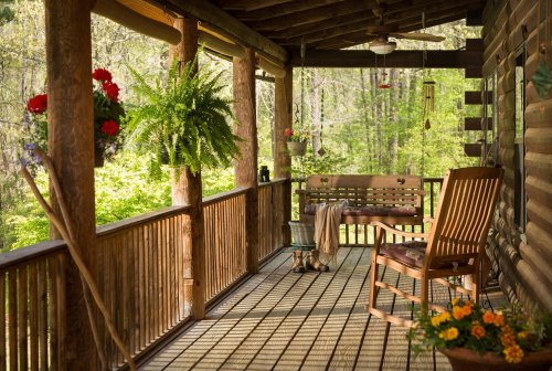 A cozy porch with wooden flooring, a rocking chair, potted plants, and a view of lush greenery.