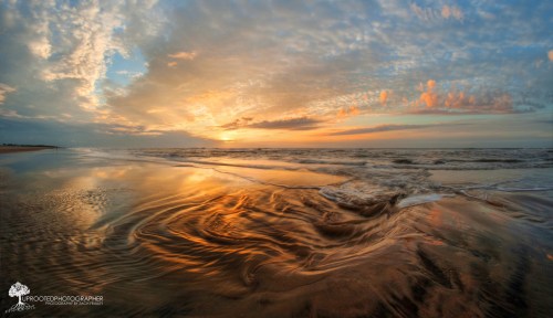A serene beach at sunset, with vibrant colors reflecting on the wet sand and gentle waves lapping at the shore.