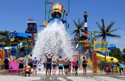A water park scene with people enjoying a large water slide and a splash zone under a clear blue sky.