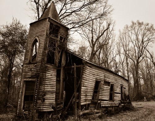 A dilapidated wooden church, leaning and overgrown, surrounded by bare trees in a desolate landscape.