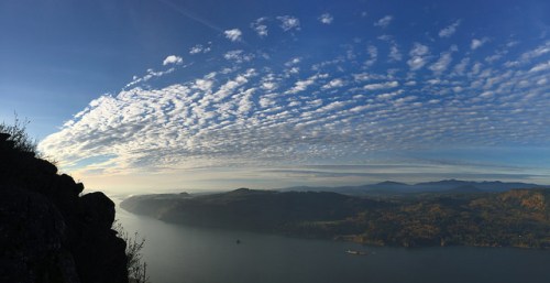 A panoramic view of a river valley under a blue sky with wispy clouds and distant mountains.