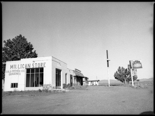 Abandoned storefront of Millican Store, featuring old signage and a desolate landscape in black and white.