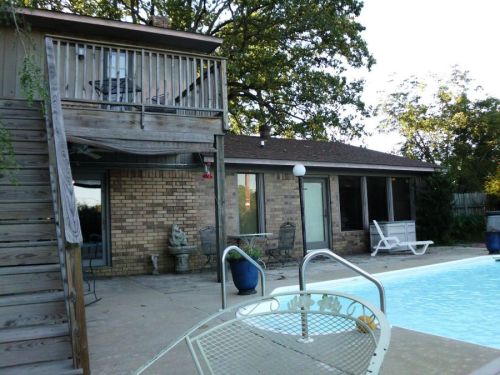 A backyard scene featuring a pool, a two-story house, and a patio area with outdoor furniture.