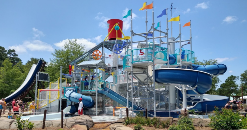 A colorful water park structure with slides, flags, and people enjoying the attractions on a sunny day.